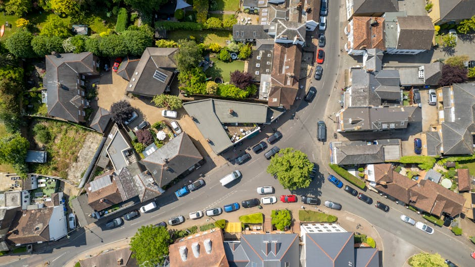 An aerial view of a narrow residential street in Kingston upon Thames showing parked cars lining both sides of the road, with a variety of houses and buildings with different roof styles including til